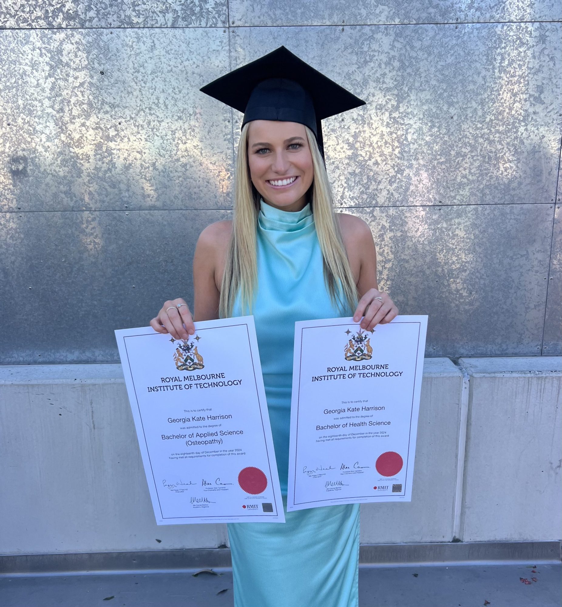 Graduate osteo georgia, wearing a blue dress, holding her 2 graduate certificates.